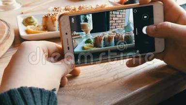 青少年的手在智能手机上制作食物的照片。 背景上日本料理的寿司卷